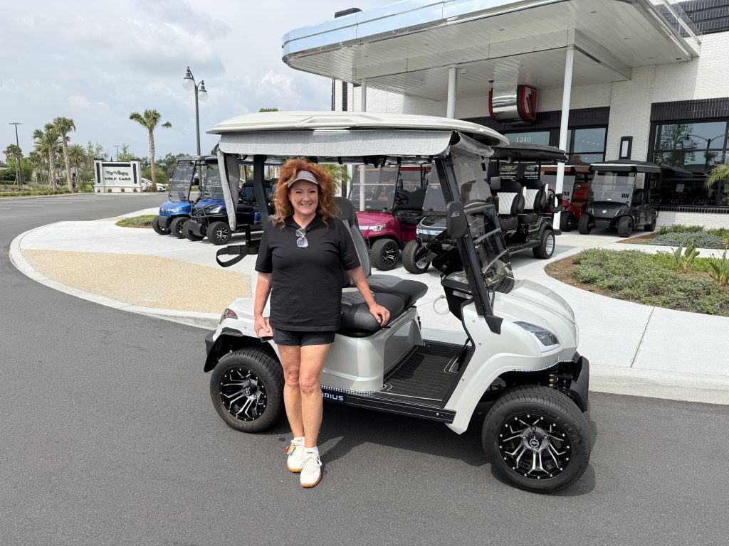 Tammi Montgomery beside an electric Star Sirius golf cart at The Villages Golf Cars, Eastport Town Square, The Villages, Florida